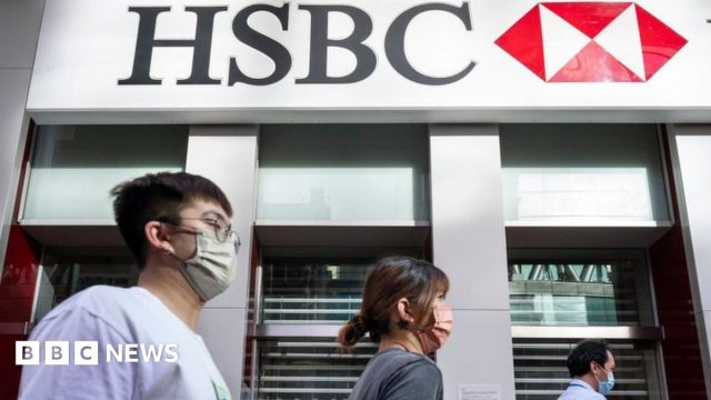 Hsbc 2022 Fca Money Laundering HSBC headquarters entrance with London City workers passing penalty headlines on phone screens.